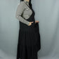 A woman modeling a black tiered jumper dress over a black and white striped long-sleeve turtleneck, standing against a light gray studio backdrop.