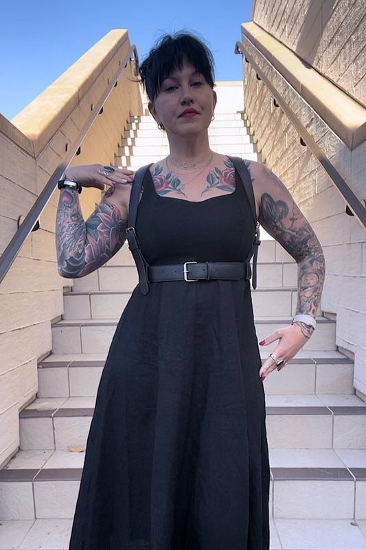 woman with tattoos on stairs in black dress and leather fashion harness
