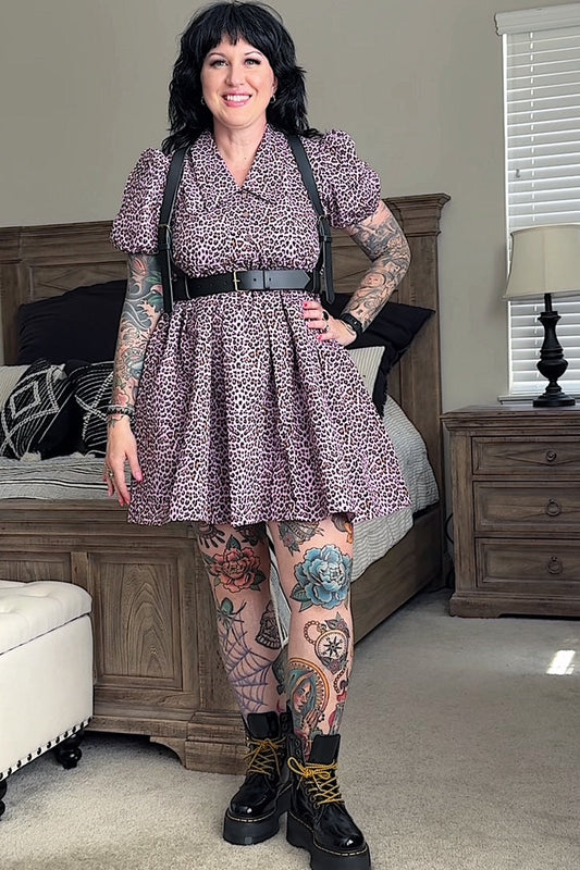 Woman in a patterned dress with suspenders standing in a bedroom.