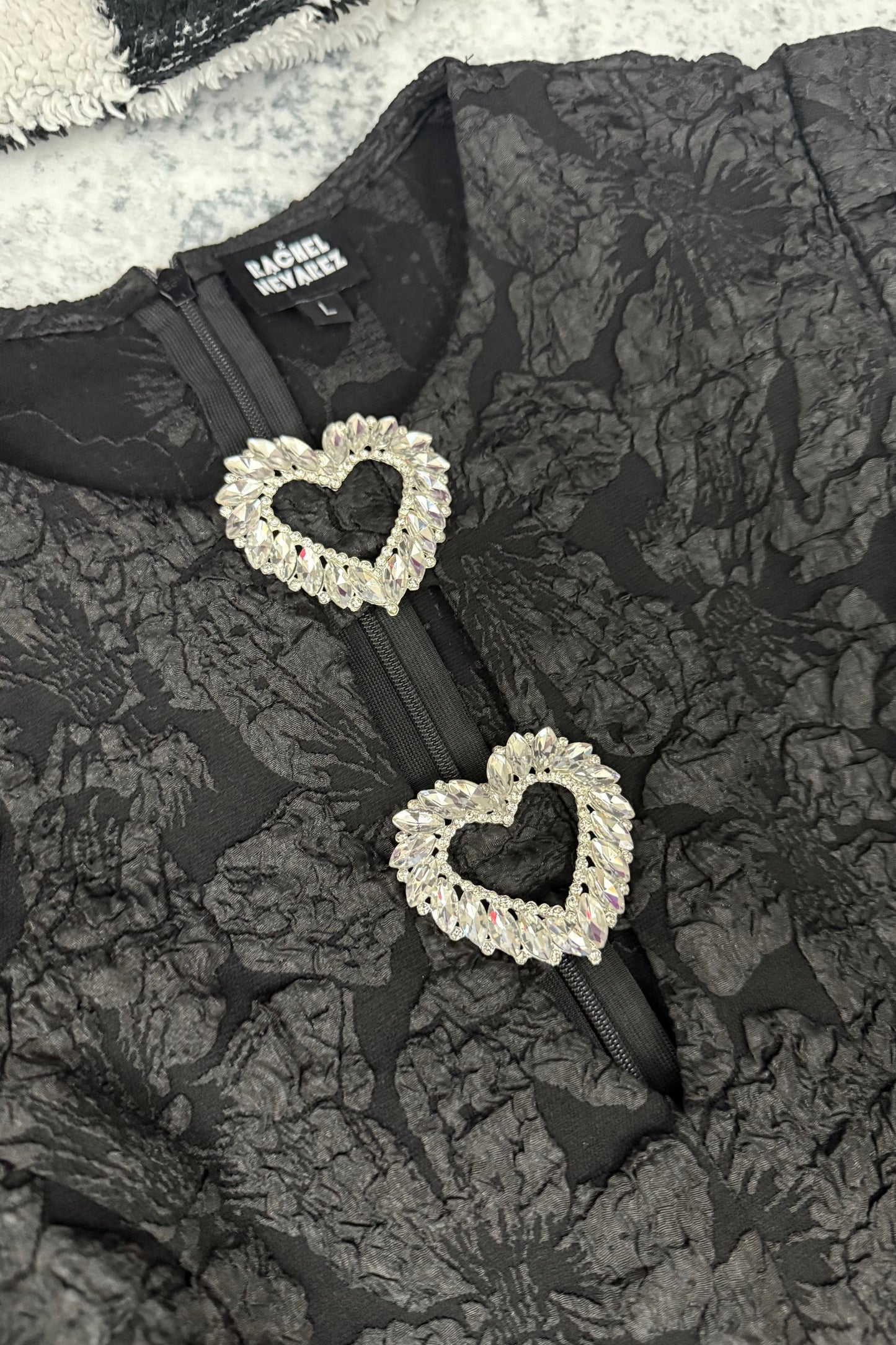 Black floral-patterned bag with heart-shaped embellishments on a textured surface