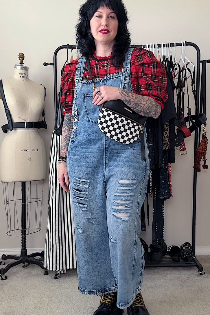 Person wearing a red plaid shirt, blue denim overalls, and black boots in a clothing store.