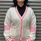 Person wearing a white cardigan with pink trim against a metallic background
