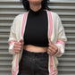 Woman wearing a white cardigan with red stripes, black top, and dark jeans in front of a metal shutter.