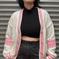 Person wearing a white cardigan with pink accents against a metallic background