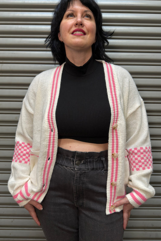 Person wearing a white cardigan with pink accents against a metallic background