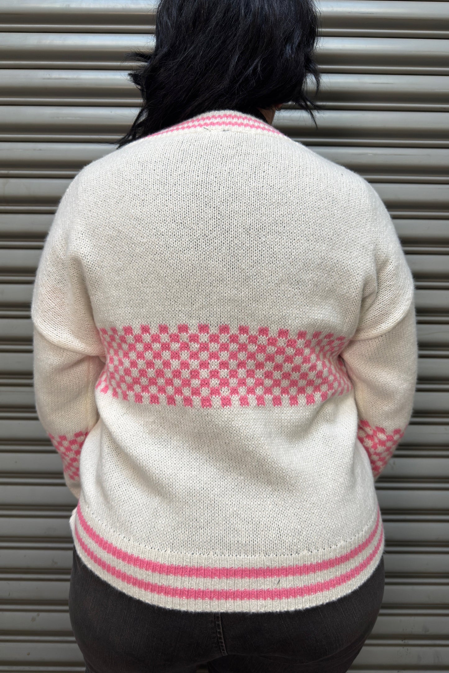 Person wearing a cream sweater with pink patterns against a metallic shutter background