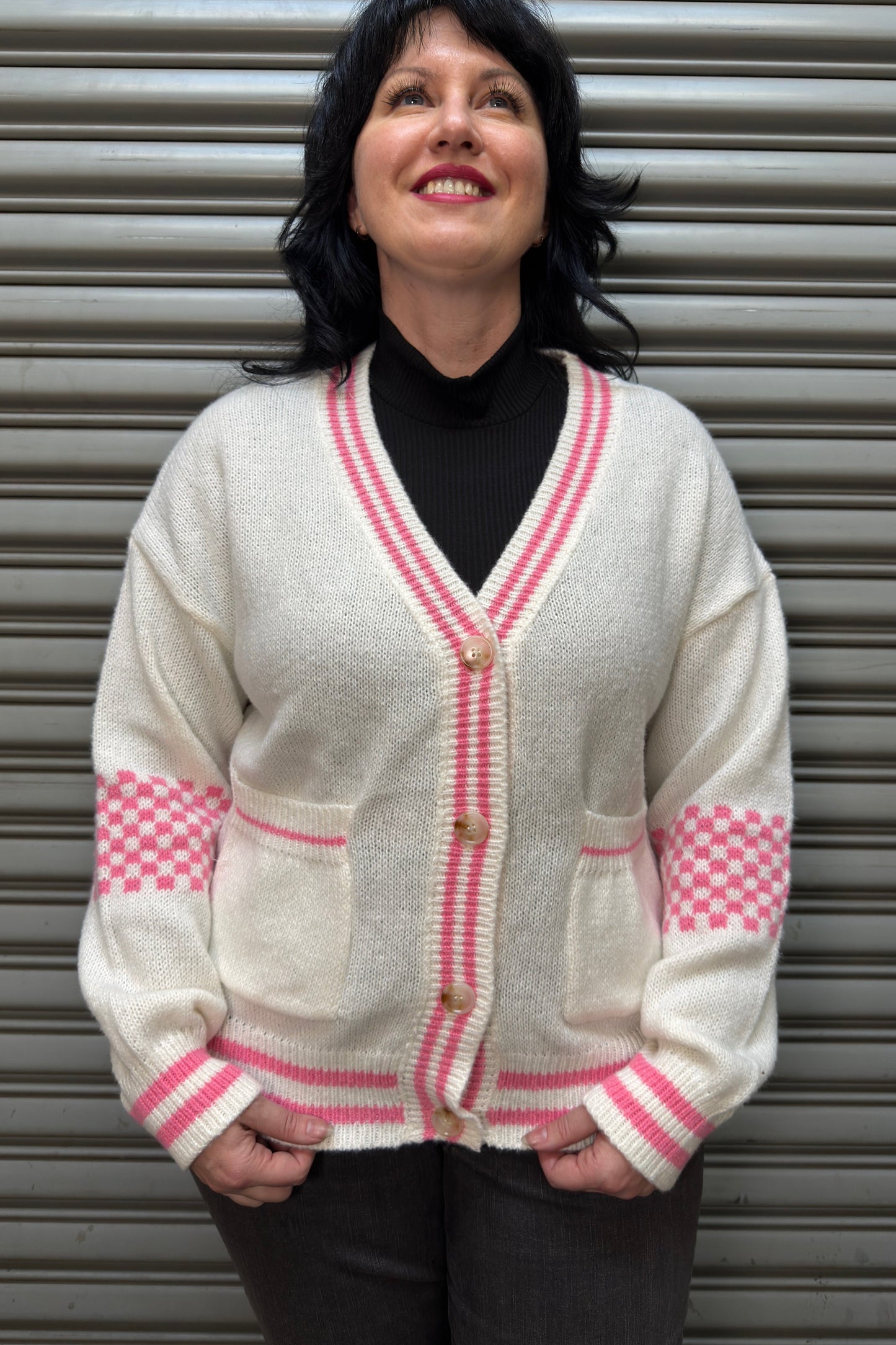 Person wearing a white cardigan with pink trim against a metallic background