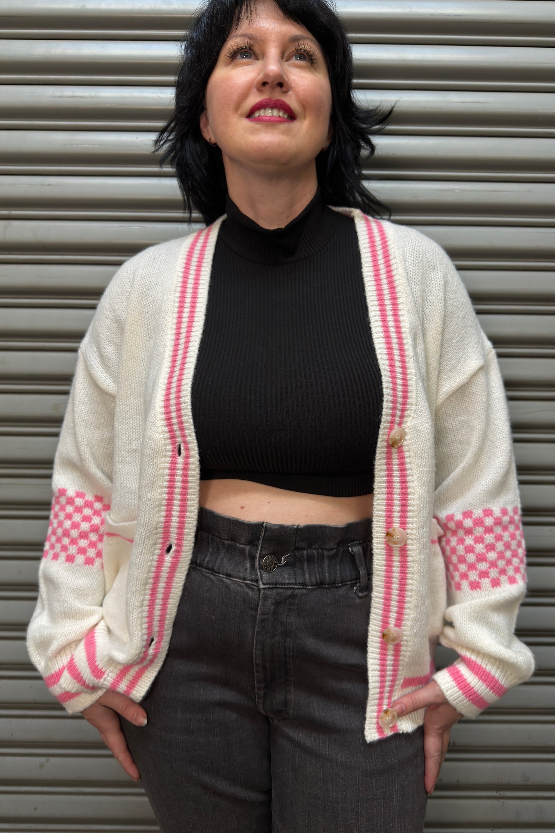 Person wearing a white cardigan with pink accents against a metallic background