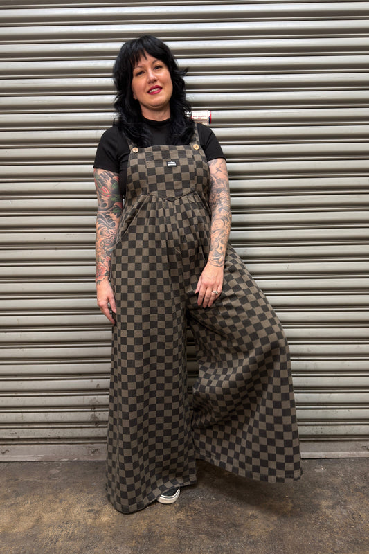 Person wearing a checkered overalls standing in front of a metal shutter.