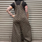 Person wearing a checkered overalls standing in front of a metal shutter.