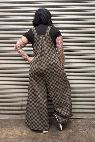 Person wearing a checkered overalls standing in front of a metal shutter.