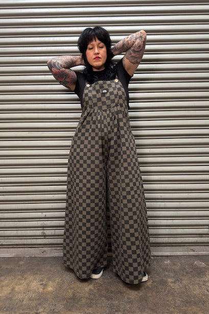 Person wearing checkered overalls standing against a metal shutter.