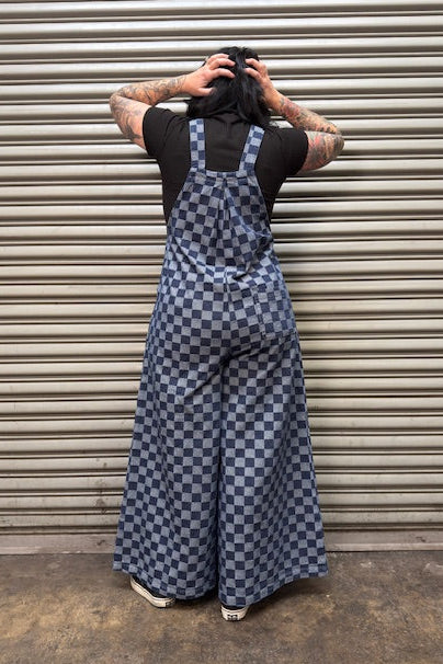 Person wearing a blue checkered jumpsuit standing in front of a metallic shutter.