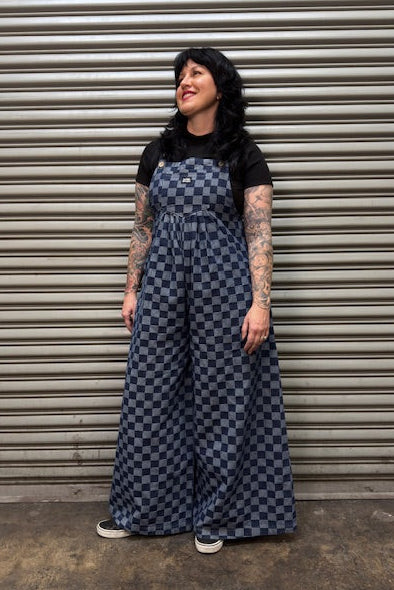 Person wearing a checkered jumpsuit standing in front of a metal shutter.