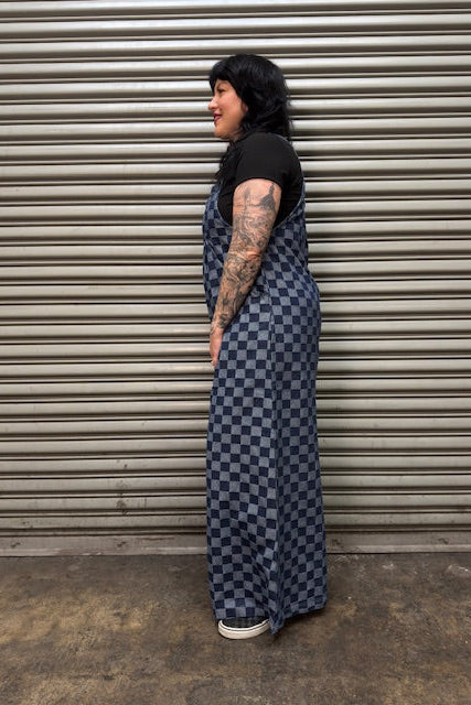 Person wearing a long blue and white checkered dress standing against a metal shutter.