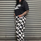 Person wearing a black t-shirt with white text and checkered pants standing against a metal shutter.