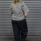 Person wearing a black and white checkered shirt and black pants standing in front of a gray metal shutter.