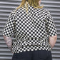 Person wearing a black and white checkered shirt against a metallic background