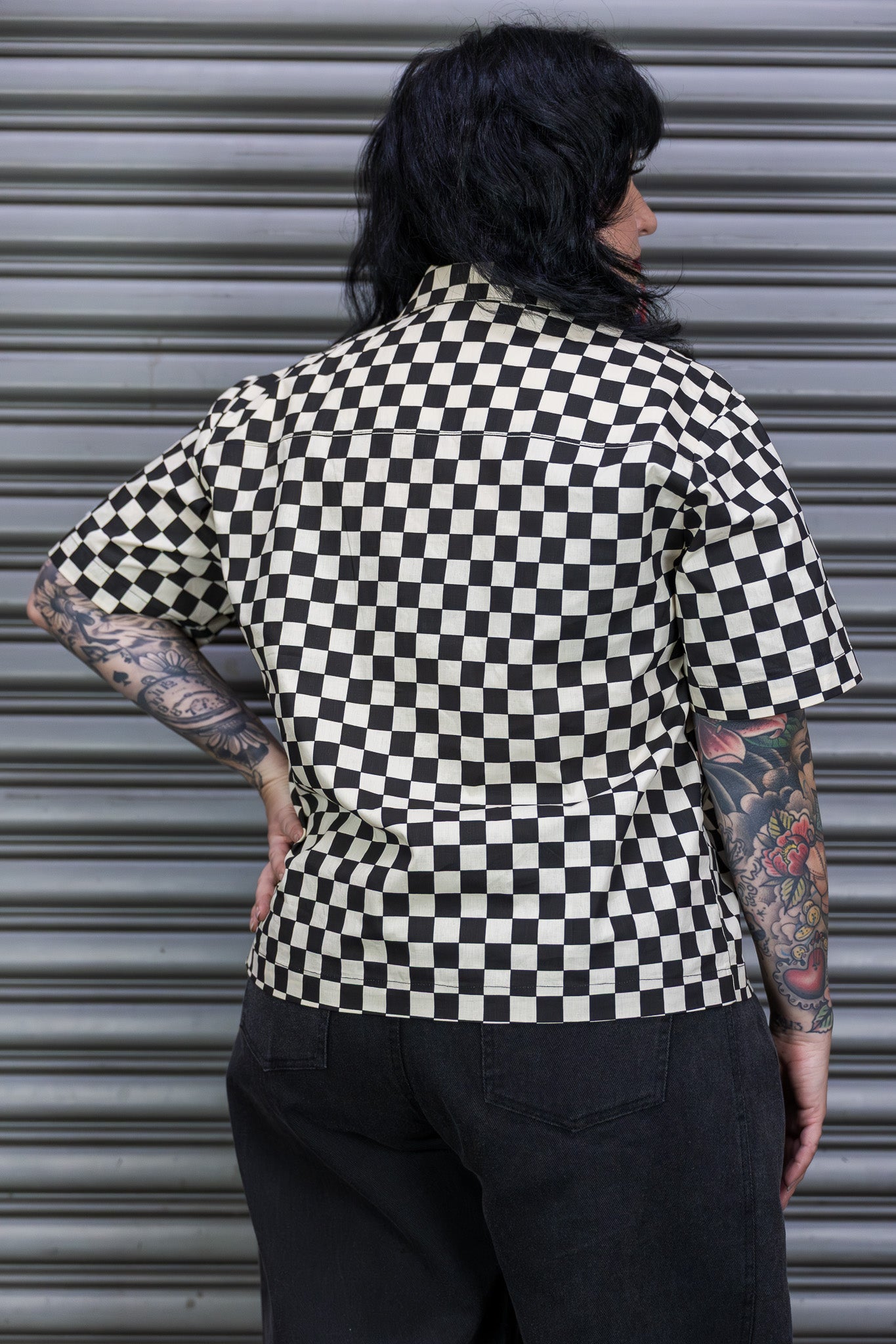 Person wearing a black and white checkered shirt in front of a metallic shutter.