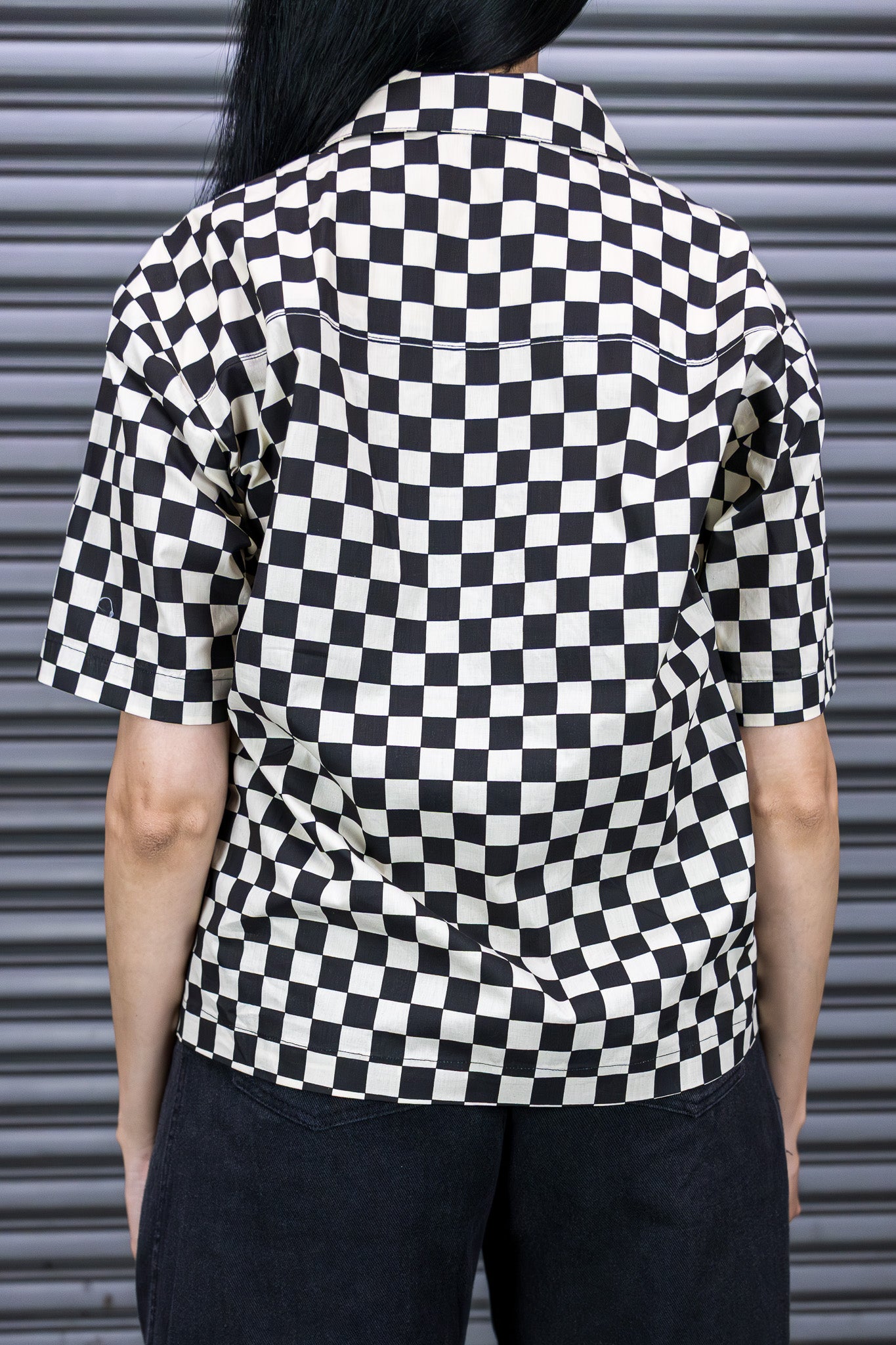 Person wearing a black and white checkered shirt against a metallic shutter background