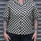 Person wearing a black and white checkered shirt with tattoos visible on arms, standing against a metallic shutter.
