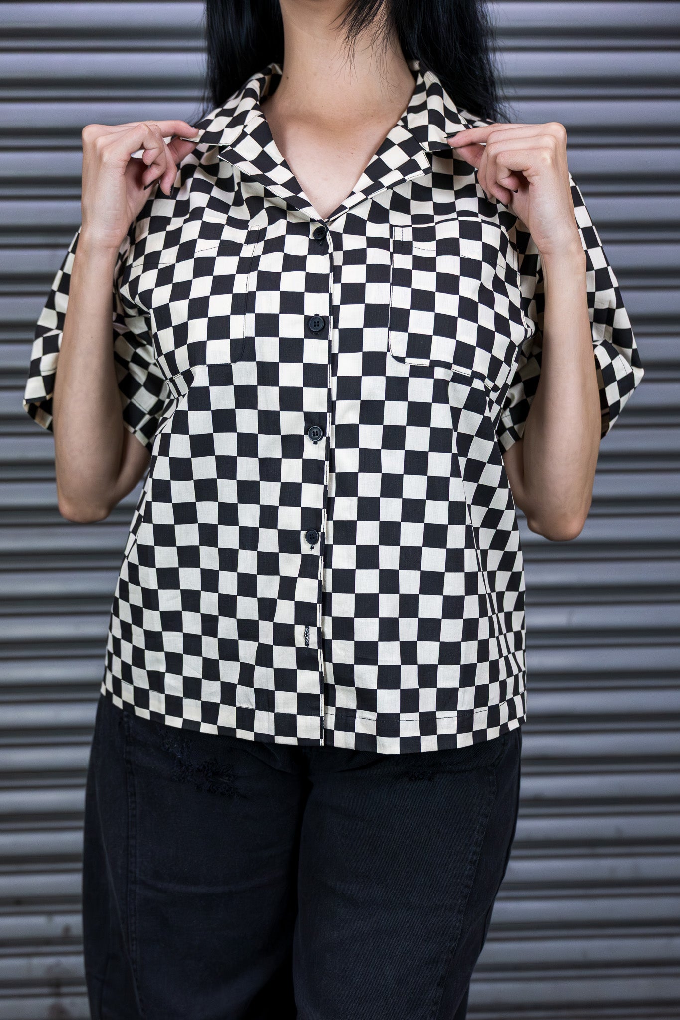 Person wearing a black and white checkered shirt against a metallic shutter background