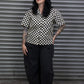 Person wearing a black and white checkered shirt standing in front of a metal shutter.