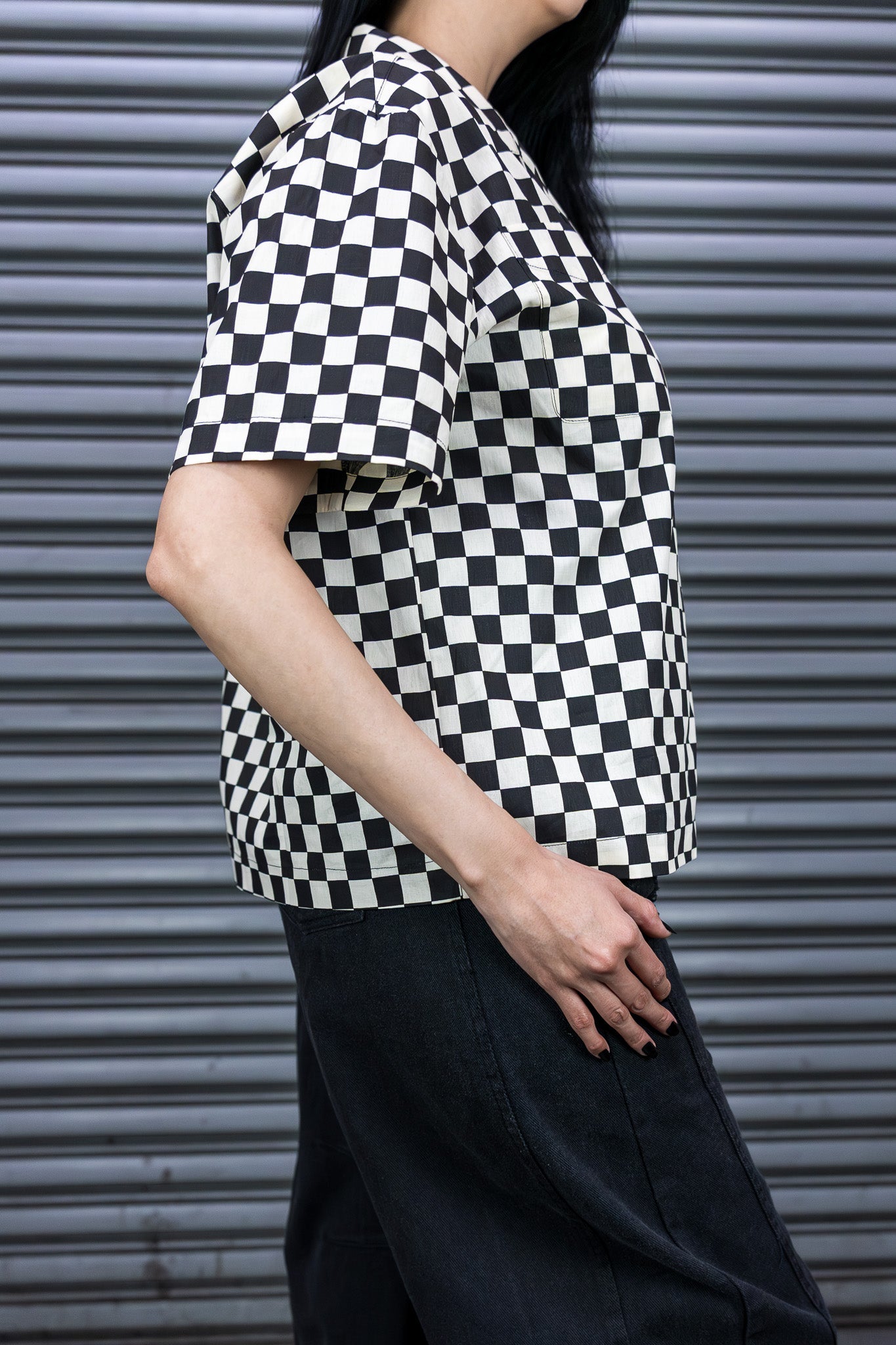 Person wearing a black and white checkered shirt against a metallic shutter background