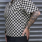 Person wearing a black and white checkered shirt with tattoos, standing in front of a metallic shutter.
