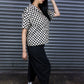 Person wearing a black and white checkered shirt with black pants in front of a metallic shutter.