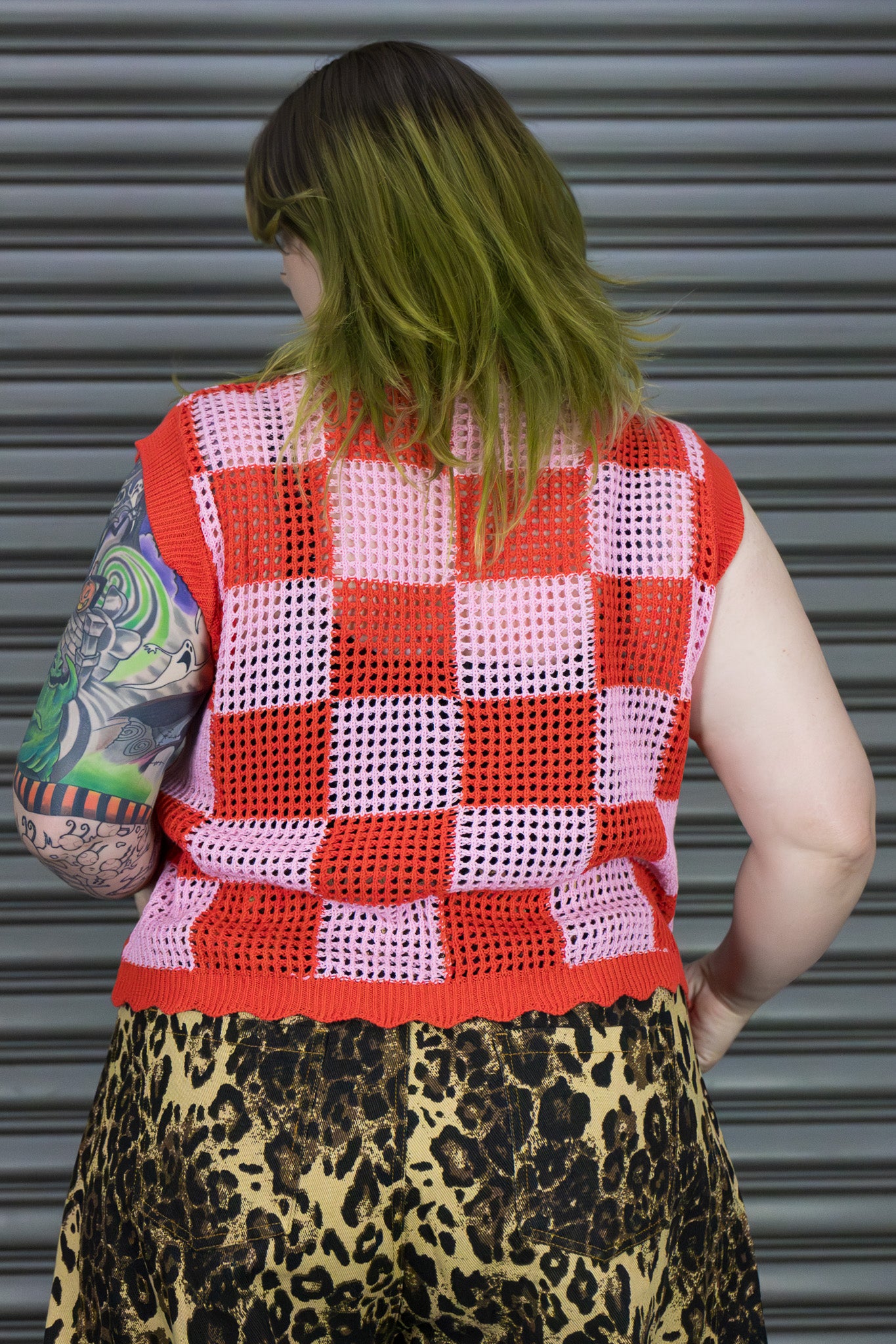 Person wearing a red and pink checkered vest with leopard print pants against a metallic background