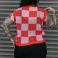 Person wearing a red and pink checkered crochet vest against a metal shutter background