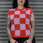 Person wearing a red and pink checkered sleeveless top against a metallic shutter background