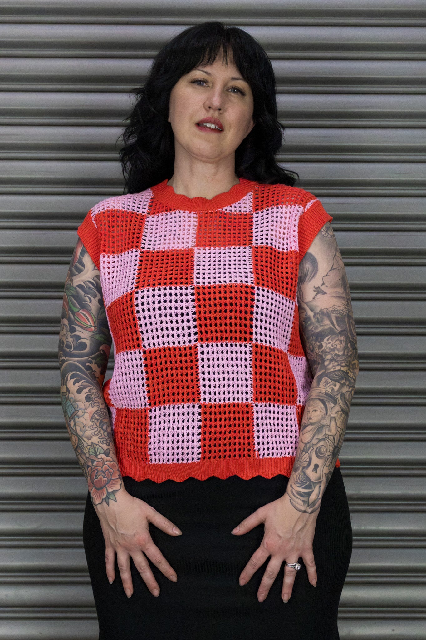 Person wearing a red and pink checkered sleeveless top against a metallic shutter background