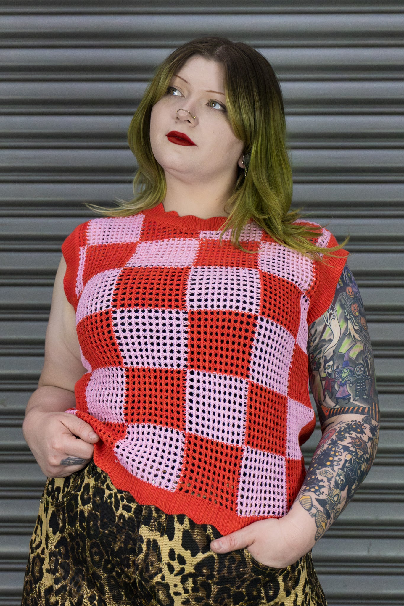 Person wearing a red and pink checkered sleeveless top with a leopard print skirt against a metallic shutter background.