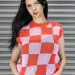 Woman wearing a red and pink checkered sleeveless top against a metallic shutter background