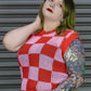 Person wearing a red and pink checkered sleeveless top with leopard print pants against a metallic shutter background.