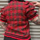 Person wearing a red plaid jacket with ruffled sleeves against a metallic background
