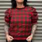 Woman wearing a red plaid top with puffed sleeves against a metal shutter background