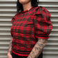 Person wearing a red plaid top with puff sleeves against a metallic shutter background