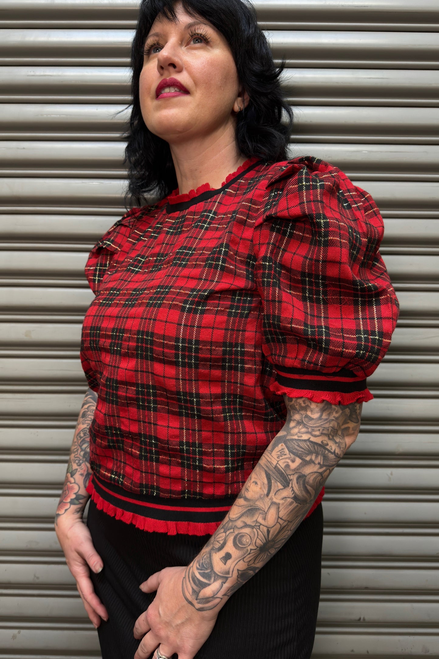 Person wearing a red plaid top with puff sleeves against a metallic shutter background