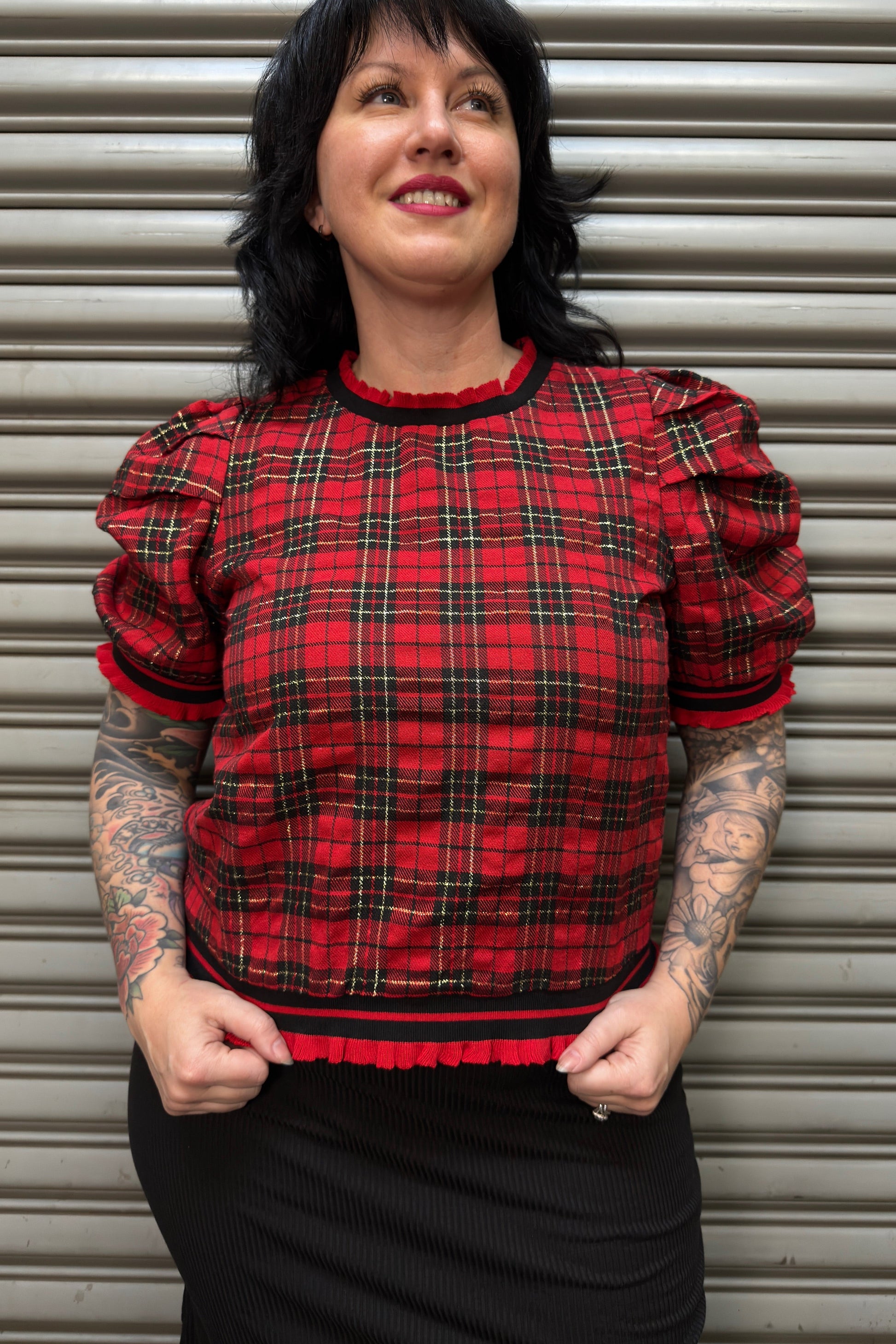 Woman wearing a red plaid top with puffed sleeves against a metal shutter background