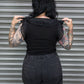 Person wearing a black top with lace details and dark pants in front of a metallic shutter.