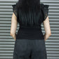 Person wearing a black top with ruffled sleeves and dark pants against a metallic shutter background