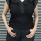 Person wearing a black sleeveless top with ruffled details against a metallic background