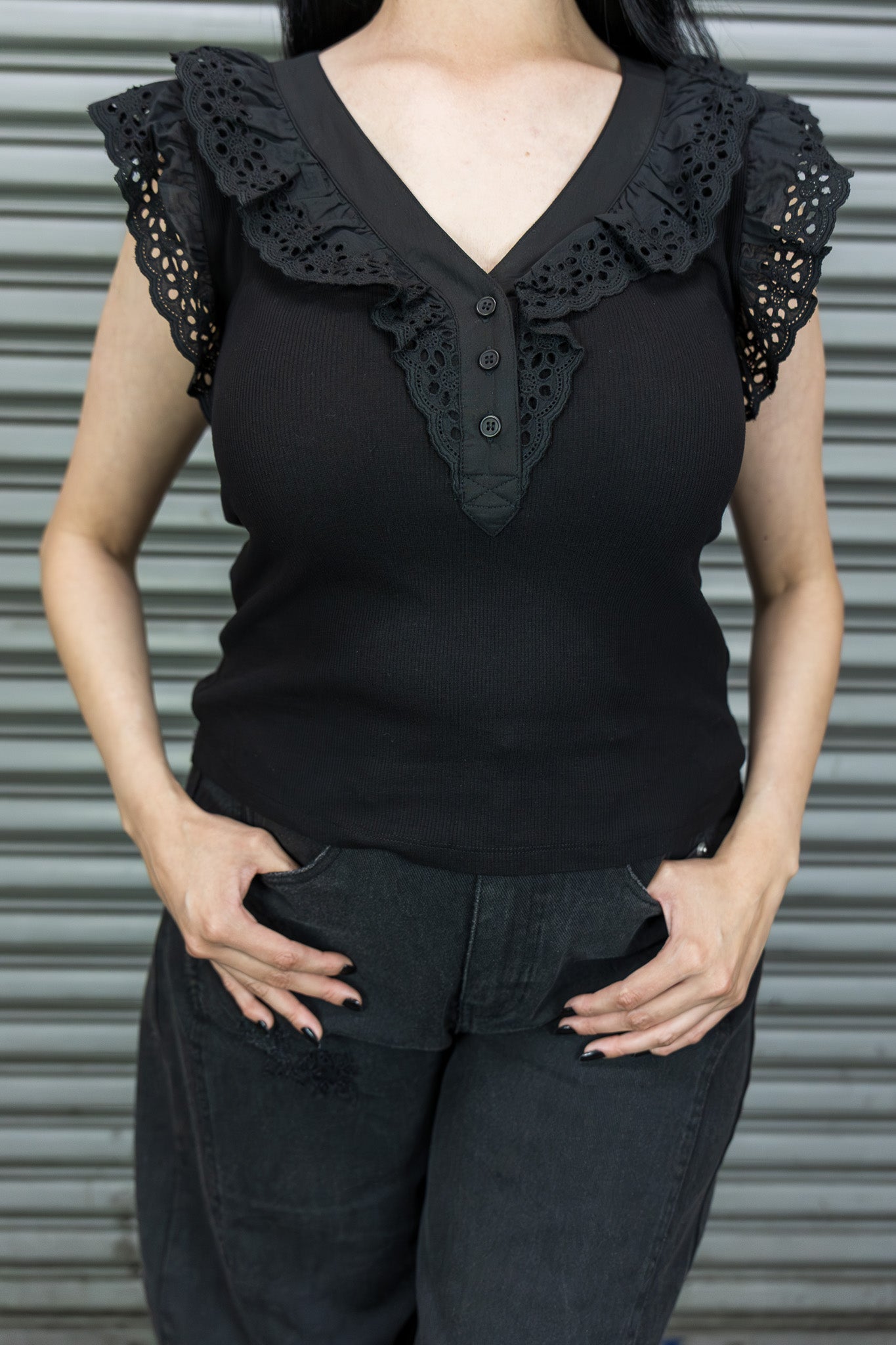 Person wearing a black sleeveless top with ruffled details against a metallic background