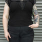 Person wearing a black sleeveless top with lace details against a metallic background