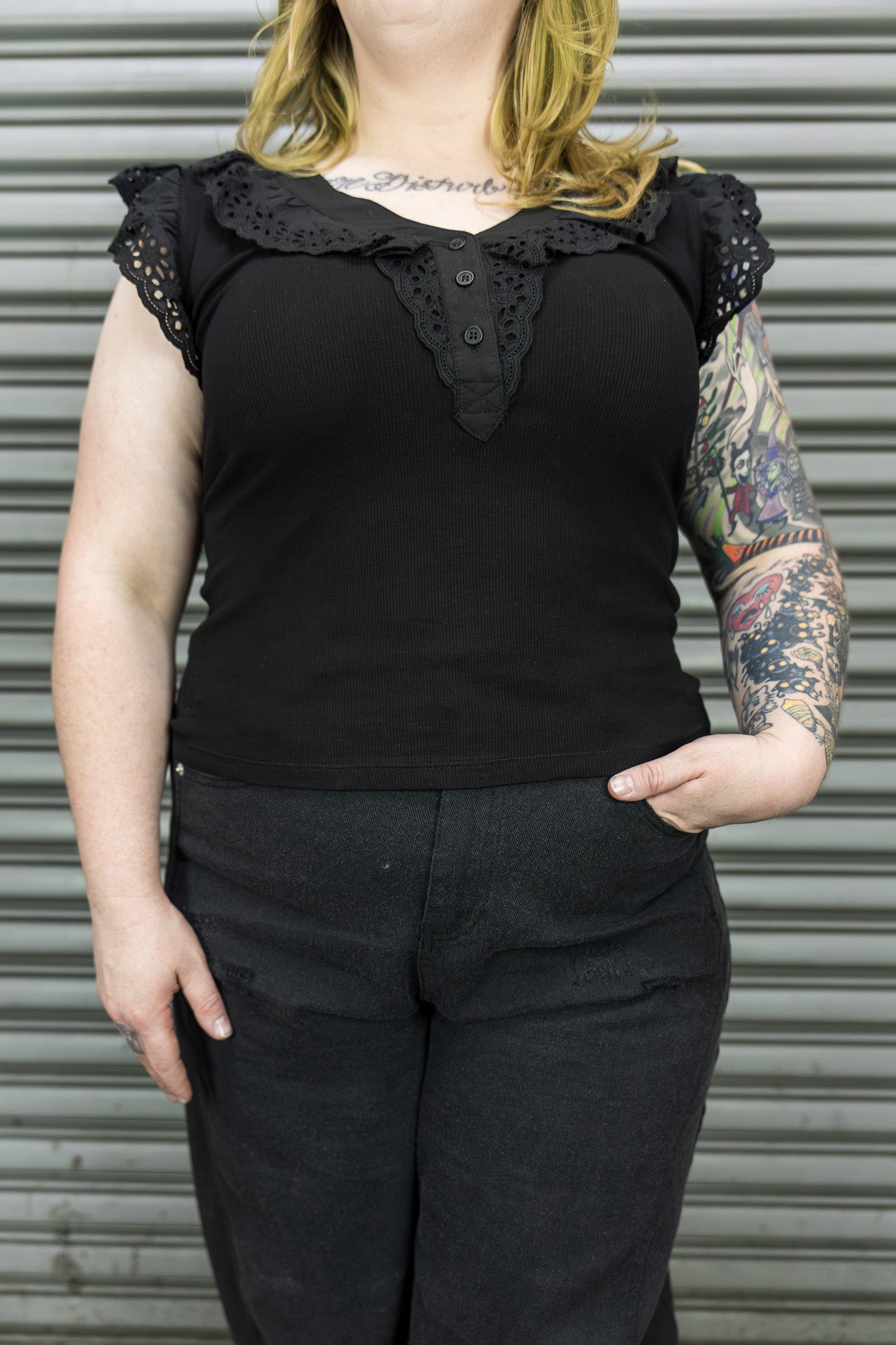 Person wearing a black sleeveless top with lace details against a metallic background