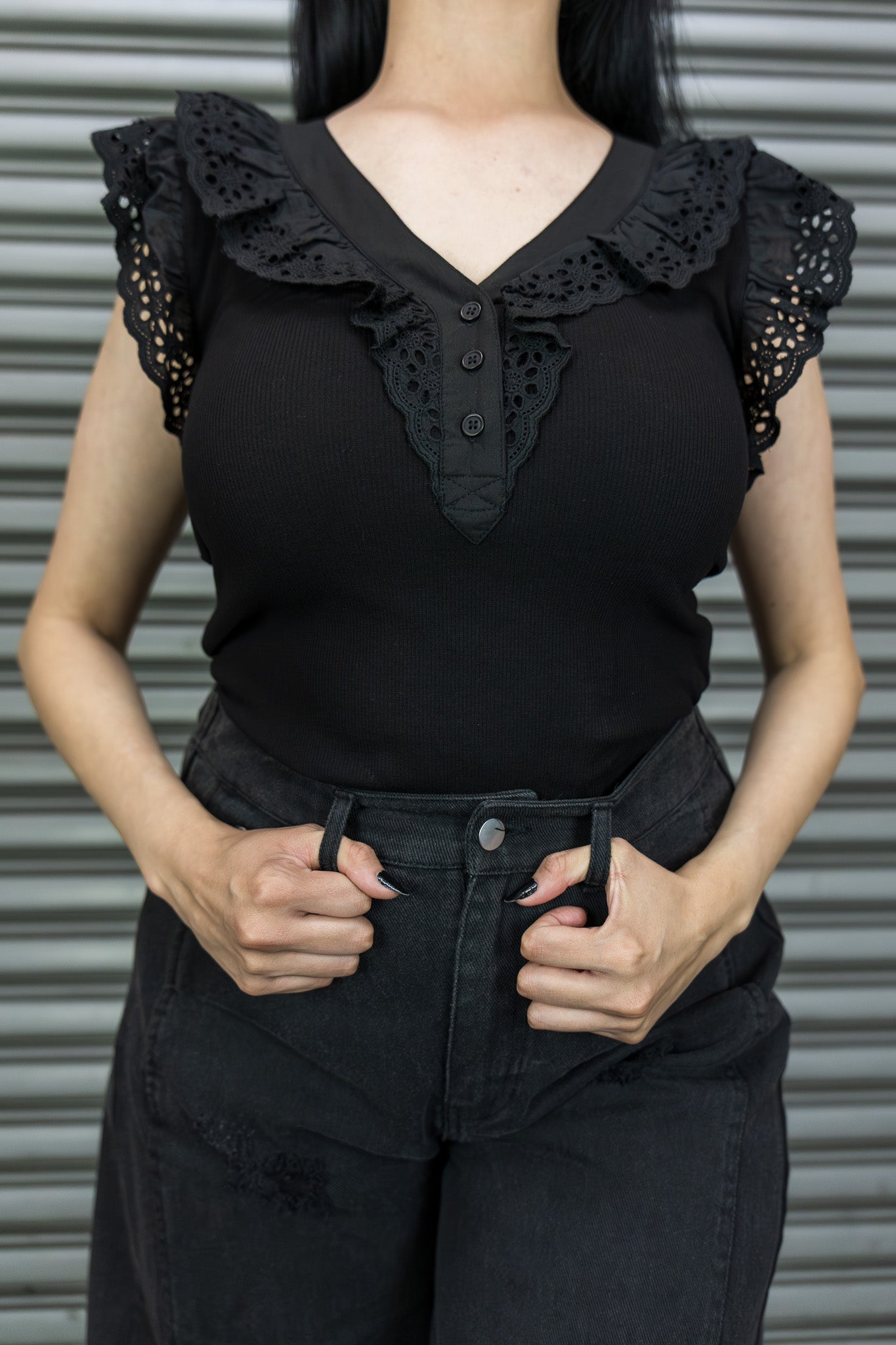 Person wearing a black sleeveless top with ruffled details against a gray background