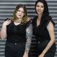 Two women in black outfits standing against a metallic shutter.